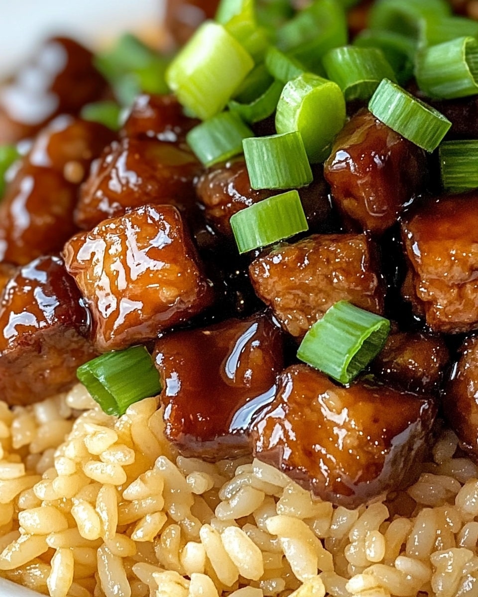 One-Pan Sweet and Tangy BBQ Sausage Rice, easy BBQ sausage rice, quick savory sausage and rice dinner, flavorful weeknight skillet meal, fuss-free sausage rice recipe The dish shows a white plate filled with fried rice mixed with small dark brown glazed meat pieces scattered evenly throughout. The rice is golden brown and shiny, with a moist and slightly sticky texture. Bright green chopped scallions are sprinkled on top, adding a fresh contrast in color and texture against the rich rice and meat. The plate sits on a white marbled surface, and the photo is taken from above to show the details clearly.