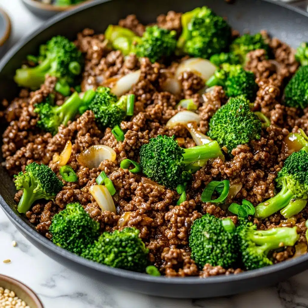 Ground Beef and Broccoli Stir Fry, Beef and Broccoli Stir Fry, Easy Beef Stir Fry, Healthy Ground Beef Dinner, Quick Weeknight Stir Fry A close-up image of a pan filled with cooked ground beef, bright green broccoli florets, and soft white onion pieces mixed together, showing a texture of crumbled meat and tender vegetables. The pan is gray and sits on a white marbled surface. In the foreground, there are small bowls with green onions and sesame seeds slightly out of focus. The food looks freshly cooked with a mix of brown, green, and white colors.