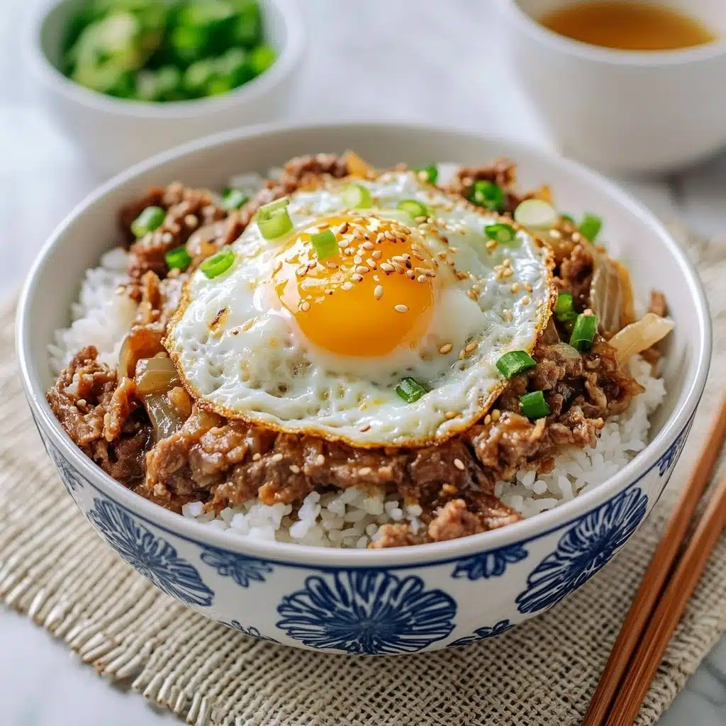 Gyudon Japanese Beef & Rice Bowls, Japanese Gyudon Recipe, Quick Gyudon Meal, Authentic Gyudon, Japanese Beef Rice Bowl A white bowl with blue flower patterns is filled with three main layers: the bottom layer is white, fluffy rice; the middle layer has cooked meat and onions mixed together, brown in color with visible green onion pieces scattered on top; the top layer is a sunny side up egg with a bright yellow yolk and white edges, sprinkled with sesame seeds and some green onion bits. The bowl is placed on a beige textured mat with a fork, chopsticks, and a small white bowl with green garnish in the background on a white marbled surface.
