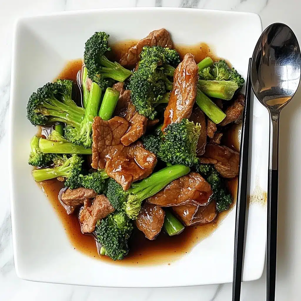 Chinese-American Beef & Broccoli, Beef & Broccoli stir-fry, homemade Beef & Broccoli, quick Chinese beef recipe, beef and broccoli dinner The dish shows slices of brown cooked beef mixed with bright green broccoli pieces and light green stalks. The beef and broccoli are covered in a shiny dark brown sauce that spreads slightly on the white square plate. To the right of the food, there is a dark wooden pair of chopsticks crossed over a metallic spoon resting on the plate. The background surface is white with a soft marbled texture.