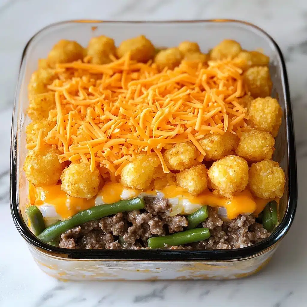 The BEST Tater Tot Casserole, Tater Tot Casserole, Easy Tater Tot Recipe, Cheesy Tater Tot Bake, Comfort Food Casserole A clear glass baking dish filled with a layered casserole. The bottom layer is melted yellow cheese mixed with green beans, visible at the edges. The top layer is a thick, even cover of golden brown, crispy tater tots, arranged tightly in rows. Some tater tots have a sprinkling of black pepper and coarse salt on them. The dish sits on a white marbled surface.