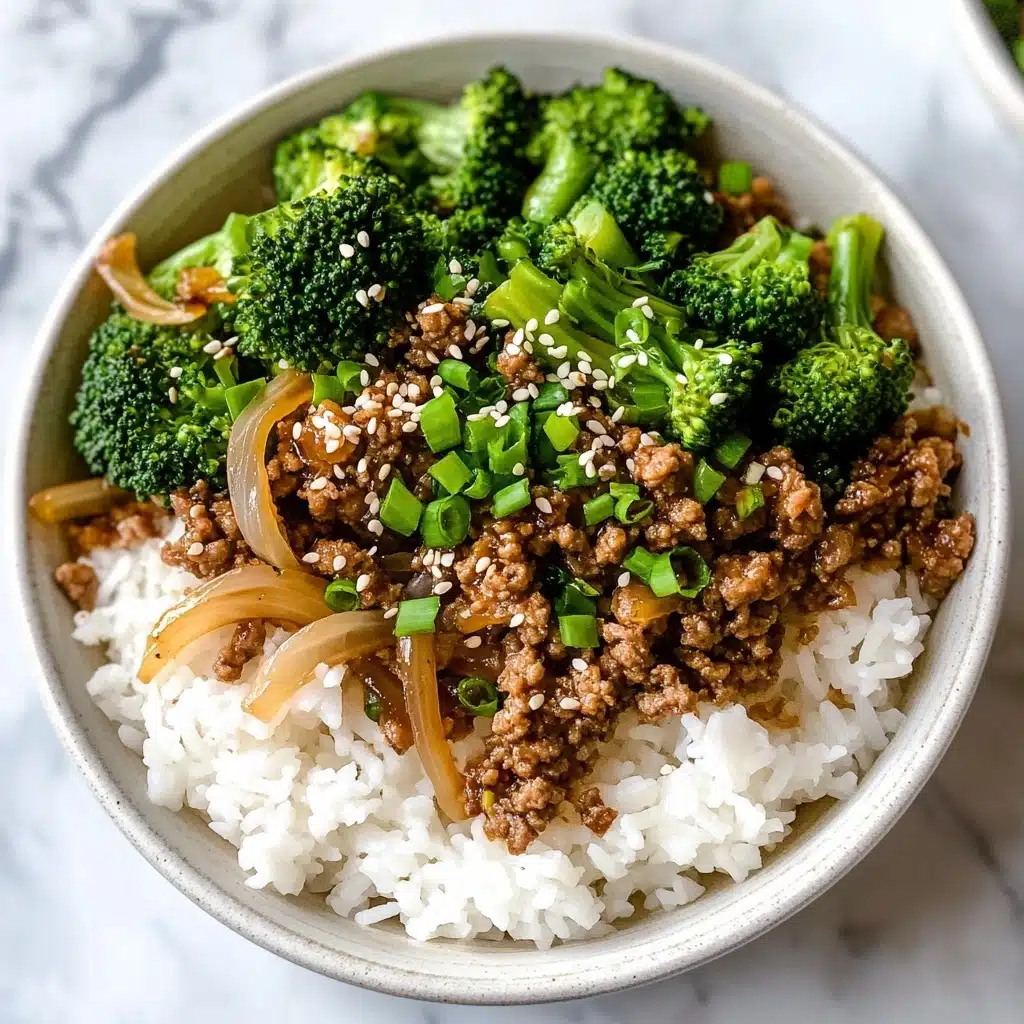 Ground Beef and Broccoli Stir Fry, Beef and Broccoli Stir Fry, Easy Beef Stir Fry, Healthy Ground Beef Dinner, Quick Weeknight Stir Fry A white bowl holds a base layer of white steamed rice with a soft, fluffy texture. On top, there is a colorful layer of cooked ground brown meat mixed with light caramelized onion pieces and bright green broccoli florets. The dish is sprinkled with small white sesame seeds and finely chopped green scallions, adding texture and color contrast. The bowl sits on a white marbled surface with soft, natural lighting enhancing the colors and textures.