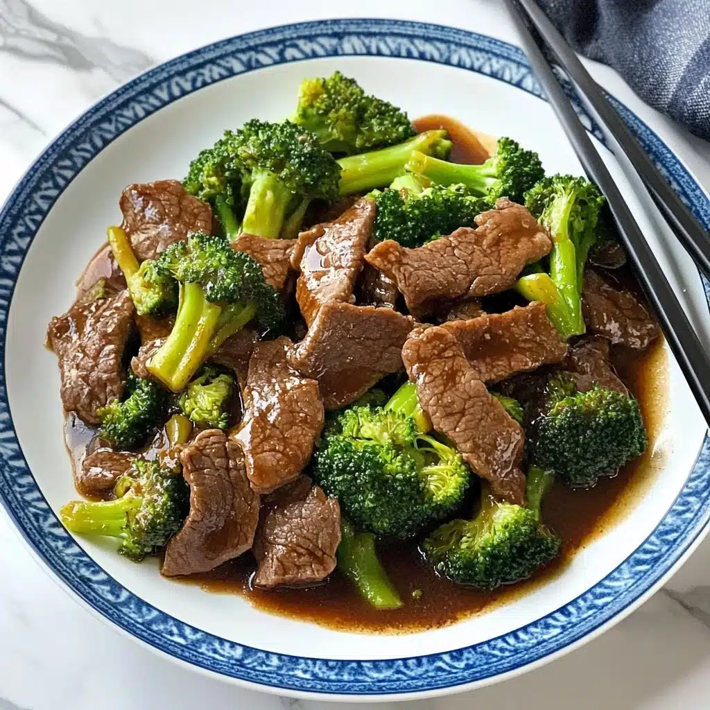 Chinese-American Beef & Broccoli, Beef & Broccoli stir-fry, homemade Beef & Broccoli, quick Chinese beef recipe, beef and broccoli dinner A white plate with a blue rim holds a dish of stir-fried beef and broccoli. The dish has two main layers: the bottom layer is a glossy brown sauce that spreads across the plate, and the top layer is made up of tender, thin slices of brown beef mixed with bright green broccoli florets. The broccoli is lightly cooked with some slightly darker green and yellow parts. A pair of silver chopsticks rests on the left side of the plate. The setting is on a white marbled surface.