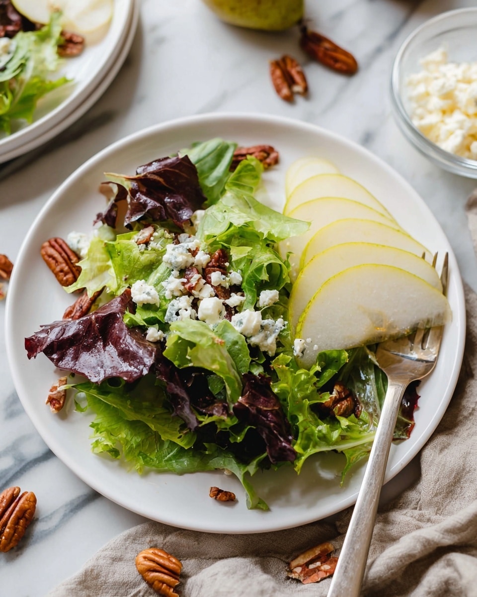 A white plate holds a simple salad with three main layers: at the bottom, mixed green and purple leafy lettuce with a wrinkled, fresh texture; above this, pale yellow-green thin slices of pear are laid neatly in a fan shape on the right side; scattered over all the layers are small white crumbles of cheese and a few whole brown pecan nuts. The plate sits on a white marbled surface with a fork resting on the right edge, a small clear bowl with more cheese crumbles nearby, and a pear and loose pecans blurred in the background. Photo taken with an iphone --ar 4:5 --v 7