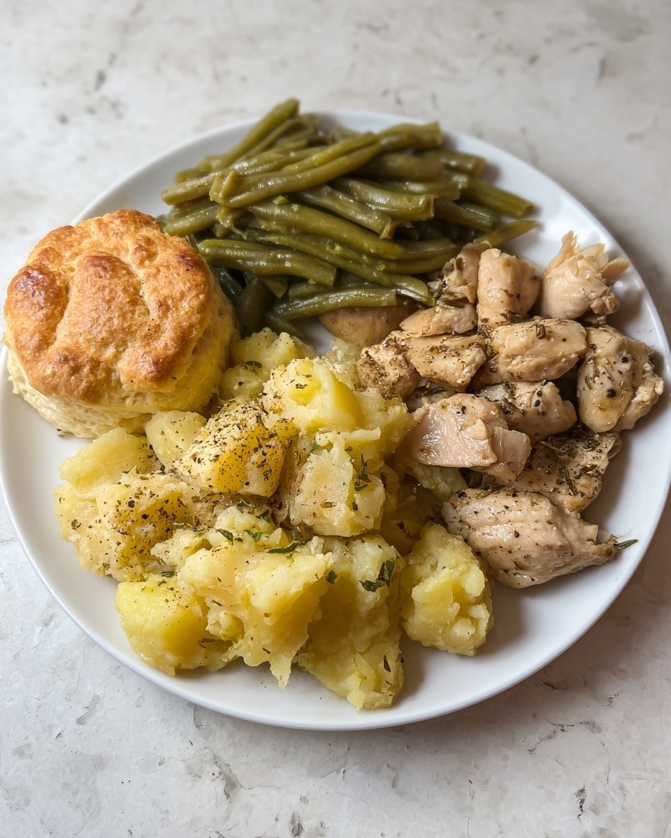 A white plate on a white marbled surface holds four food parts. At the top right, there are cooked light brown chicken pieces with some black pepper and herbs. To the left of the chicken, there is a pile of sloppy yellow smashed potatoes with black pepper sprinkled on top. Above the potatoes and chicken, there are steamed green beans stacked in a neat pile. On the left side of the plate, there is a biscuit with a golden-brown crust and soft layers visible on the side. Photo taken with an iphone --ar 4:5 --v 7