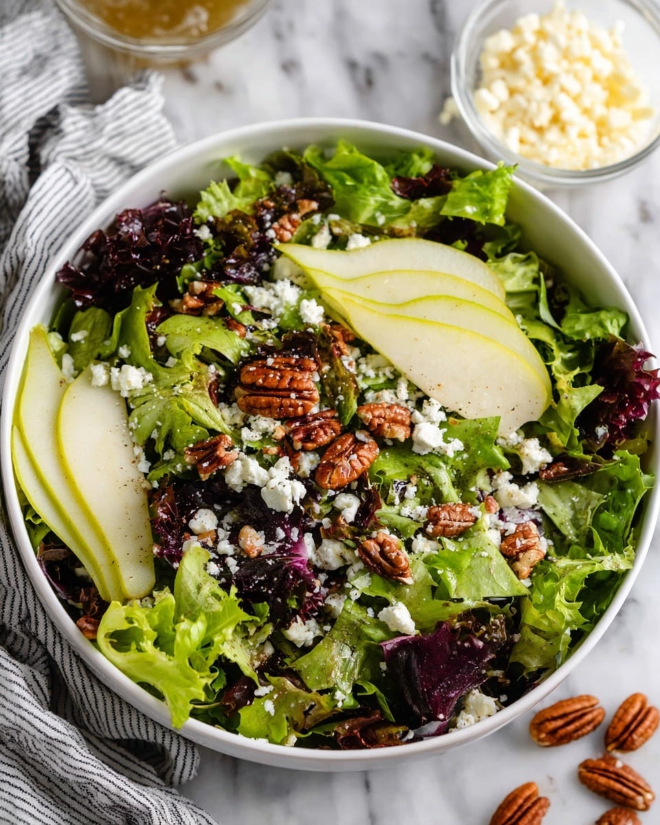 A white bowl holds a fresh layered salad starting with a base of curly and mixed green lettuce leaves that have a vibrant green and purple color and leafy texture. On top, thin slices of light green pear with smooth skin are carefully placed around the bowl. Scattered across the salad are small crumbles of white cheese that add a bit of rough texture. Finally, glossy brown pecan halves are sprinkled evenly over the top, adding a crunchy element. The bowl sits on a white marbled surface with a small glass bowl of cheese and a striped cloth napkin nearby. Photo taken with an iphone --ar 4:5 --v 7