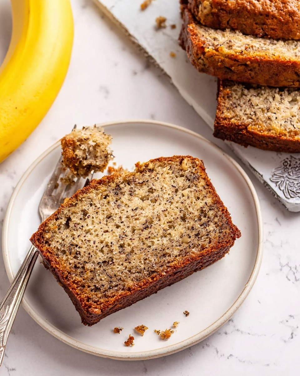 A piece of banana bread with a rough, crumbly texture and brown specks throughout sits on a white plate with small brown dots. The bread shows a golden brown crust around the edges and a lighter inside with visible mashed banana bits. A silver fork holds a smaller piece of the bread above the plate. To the right, two more thicker slices of banana bread rest partly visible on a white marbled surface beside a whole yellow banana and a silver butter knife. The scene is brightly lit and simple. photo taken with an iphone --ar 4:5 --v 7