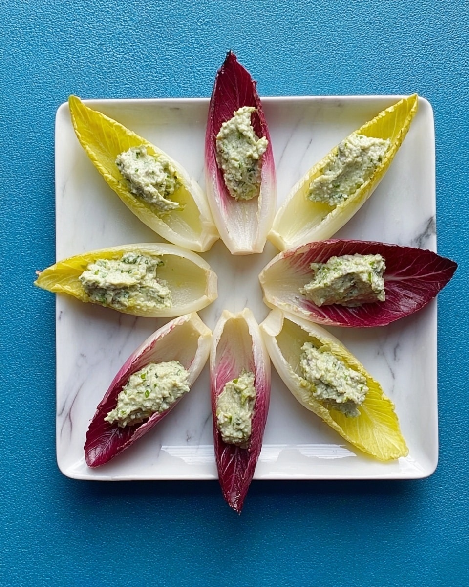 A square white plate with six leaves arranged in a circle, alternating between yellow and red endive leaves. Each leaf holds a dollop of light green creamy dip with a slightly chunky texture. The plate is placed on a white marbled surface with a blue fabric underneath. The scene is viewed from above, showing all layers clearly. photo taken with an iphone --ar 4:5 --v 7