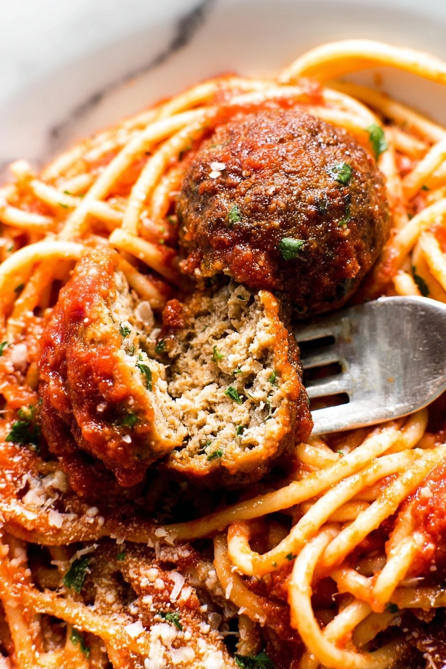 The image shows a close-up of a plate of spaghetti with tomato sauce and two meatballs, one whole and one cut in half to show its inside texture. The spaghetti is light orange with a smooth surface, coated with thick red tomato sauce that has small bits of herbs. The meatballs are brown with a slightly rough texture, and the cut meatball reveals a dense inside with green herbs mixed in. There is a sprinkling of grated cheese and chopped green herbs on top. A silver fork is placed under the cut meatball. The plate is white, and the background is a white marbled texture. photo taken with an iphone --ar 2:3 --v 7 - Spaghetti with Homemade Meatballs in Rich Tomato Sauce, homemade Italian pasta and meatballs, classic Italian spaghetti recipe, hearty tomato sauce with meatballs, family-friendly Italian dishes