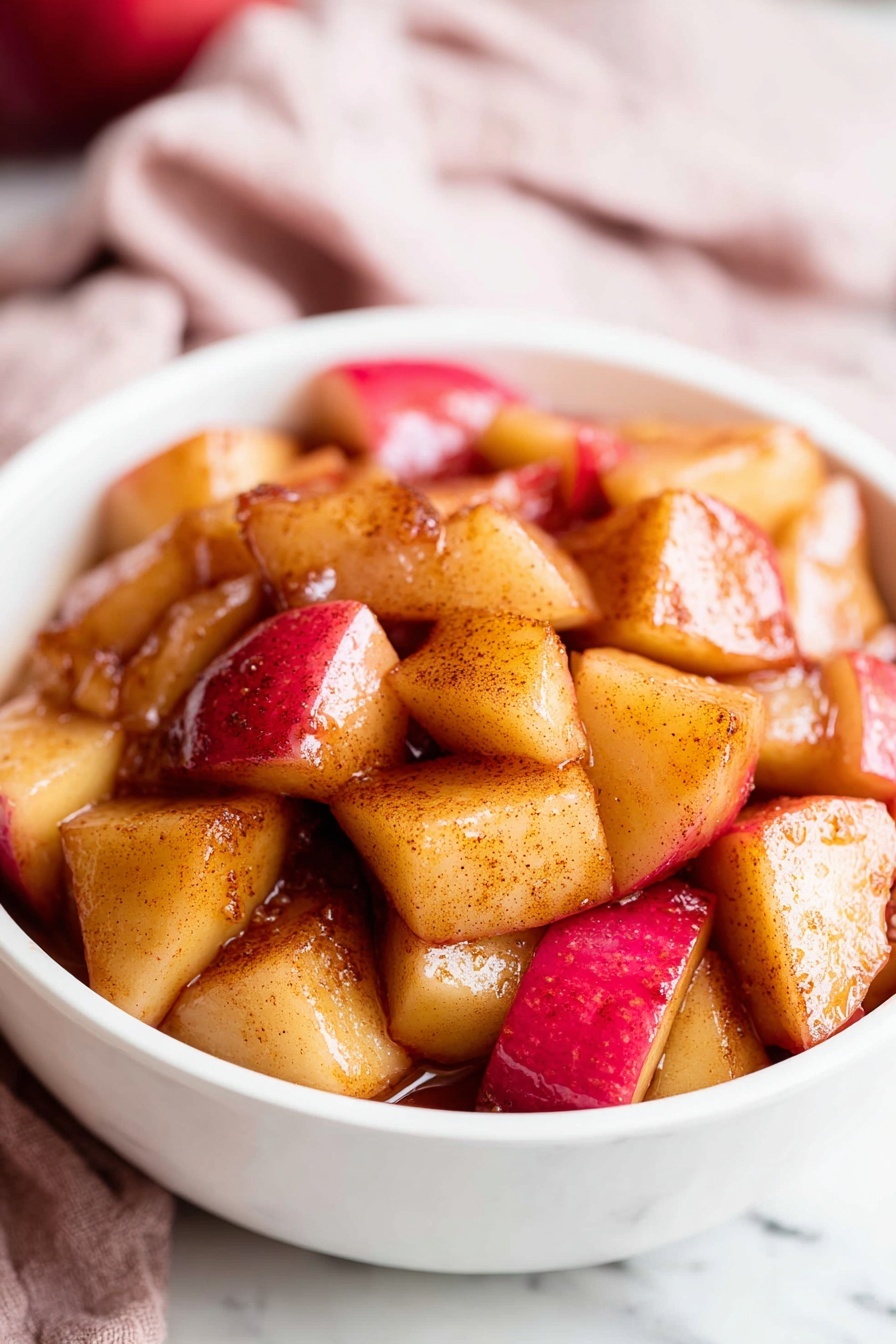 A black pan filled with evenly cooked, cubed apple pieces showing a mix of golden brown and red skin tones, lightly caramelized with a shiny texture scattered all over the pan; the pan handle is metal with visible wear and sits on a white marbled surface partially covered by a soft red and white checkered cloth. To the top right, two whole red apples rest on a small round wooden board. The image is bright and simple, focusing on the warm colors and textures of the cooked apples. photo taken with an iphone --ar 2:3 --v 7 - Easy Cinnamon Apples, cinnamon apple dessert, warm apple snack, quick apple dessert, simple apple side dish
