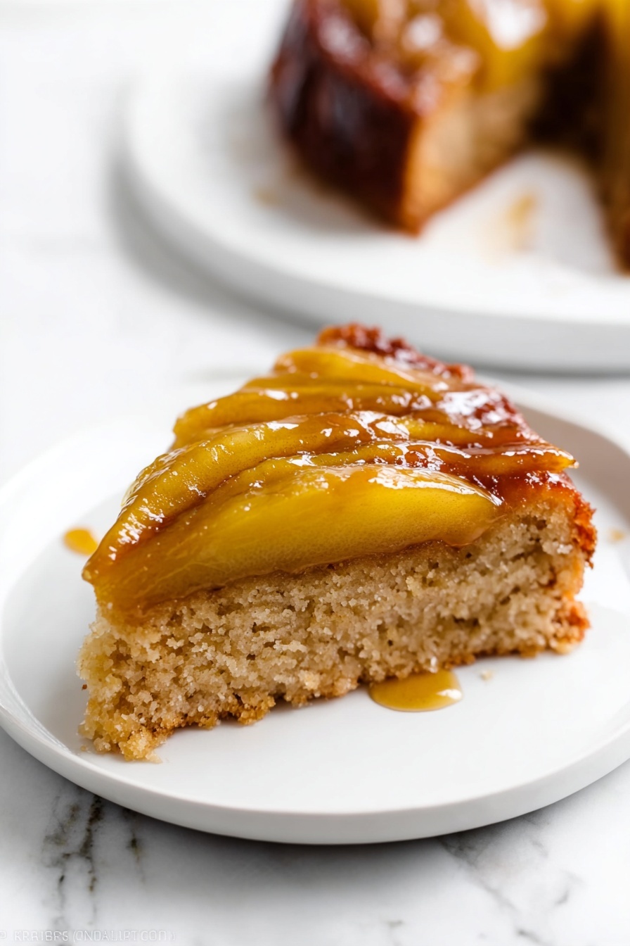 A slice of cake with two layers is shown on a white plate set on a white marbled surface. The bottom layer is a light brown, soft, and spongy cake base. The top layer has cooked apple slices that are golden-yellow and shiny with caramel glaze, creating a sticky and glossy texture. The apple slices lie flat on the cake, and some syrup has slightly dripped onto the plate. In the background, there is a blurred white plate with another piece of the same cake. Photo taken with an iphone --ar 2:3 --v 7 - Caramel Apple Upside Down Cake, fall dessert recipes, easy apple cake, caramel apple dessert, cozy autumn cake