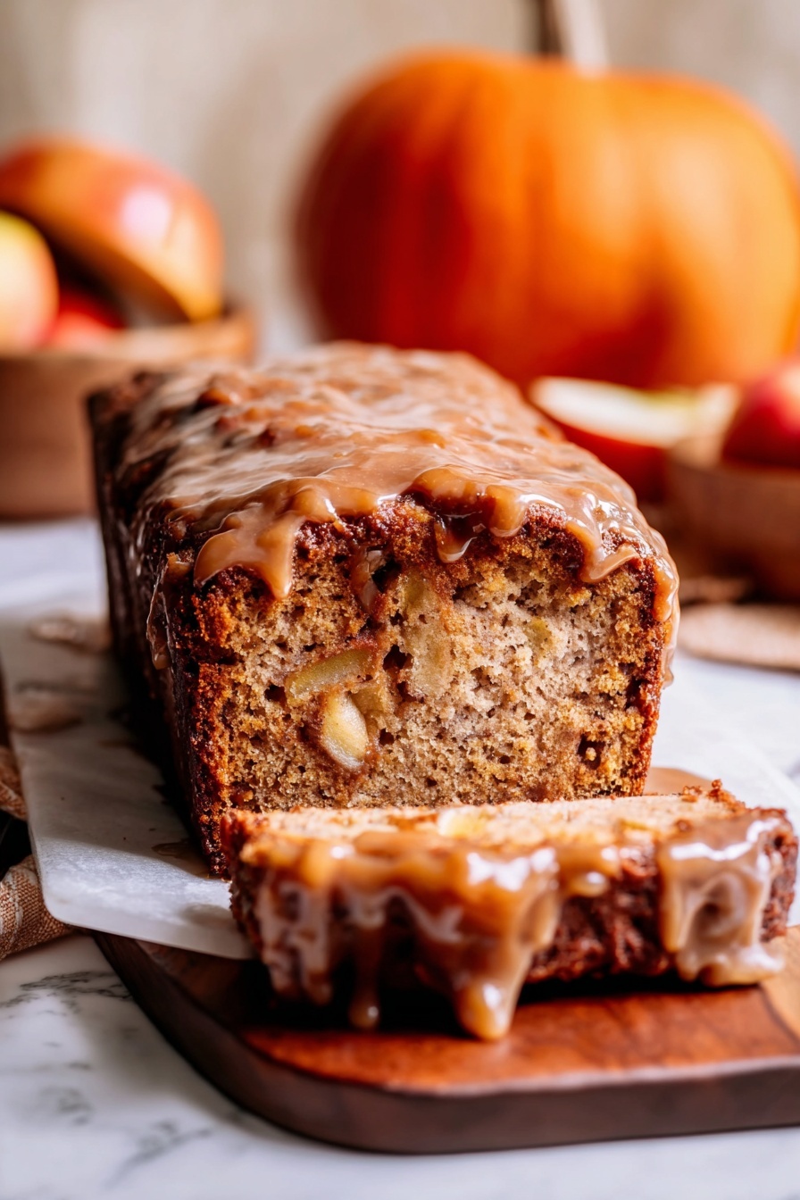 A loaf cake sits on a wooden board over a white marbled surface, sliced at the front showing its dense, light brown inside with visible chunks of apple. The top layer is a thick, sticky, darker brown glaze that drips down the sides, giving the cake a shiny look. In the background, there is a small orange pumpkin and a wooden bowl with apples that add warm tones to the image. The photo is warm and cozy, focusing tightly on the textures of the cake and glaze, with a soft, light blur in the background. photo taken with an iphone --ar 2:3 --v 7 - Amish Apple Fritter Bread, apple cinnamon quick bread, fall dessert bread, cinnamon apple bread recipe, soft sweet apple bread