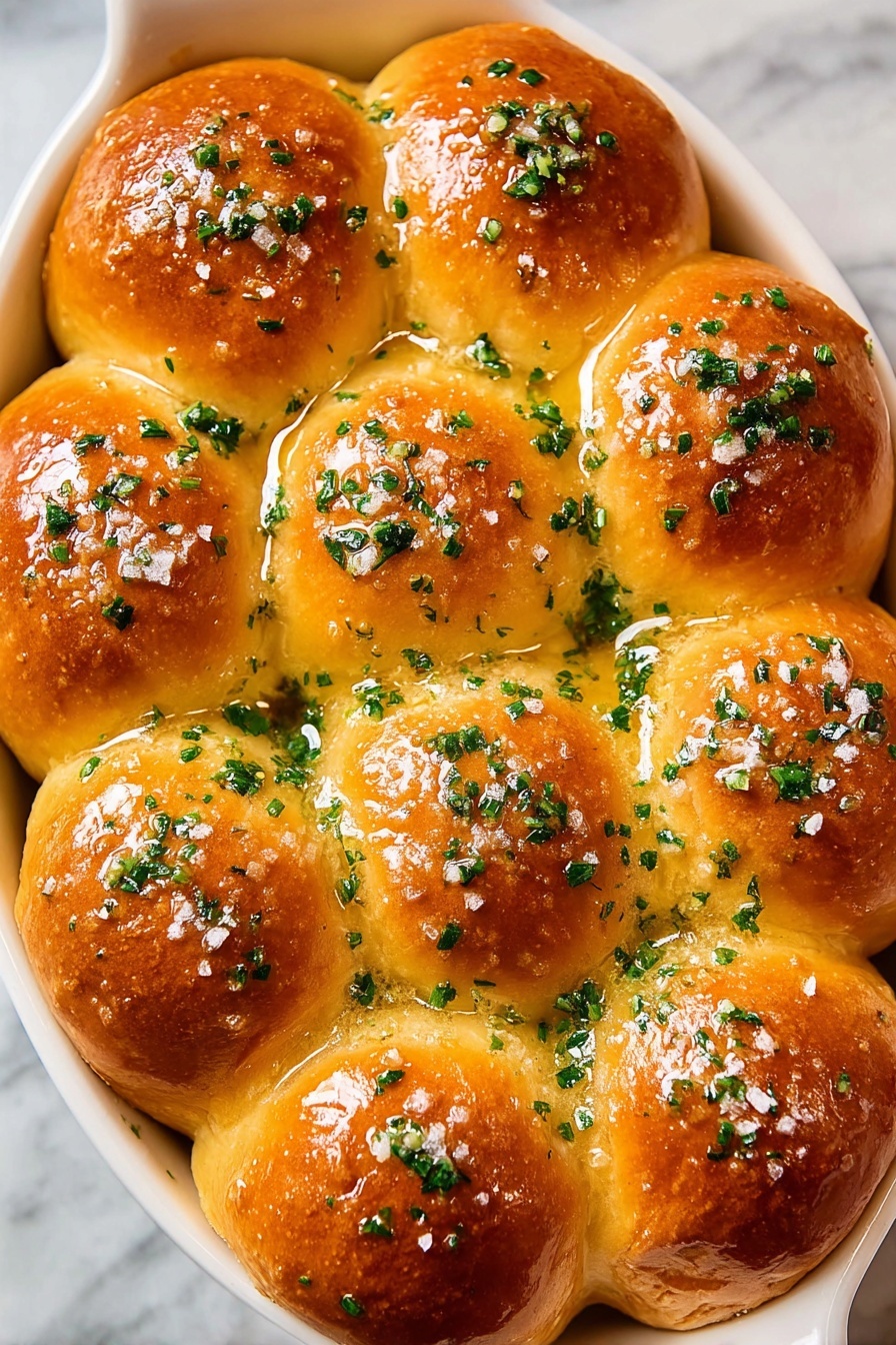 The image shows a white oval dish filled with 15 golden brown rolls arranged in a close cluster. Each roll has a smooth, shiny surface that looks soft and fluffy with a slight crisp on top. The rolls are topped with chopped green herbs spread evenly, adding fresh color contrast. There is a light glaze that makes the rolls appear moist, and small bits of coarse salt can be seen scattered on the surface. The dish is set on a white marbled texture background. photo taken with an iphone --ar 2:3 --v 7 - Garlic Butter Dinner Rolls, Fluffy Dinner Rolls, Garlic Bread Rolls, Easy Dinner Rolls, Soft Dinner Rolls