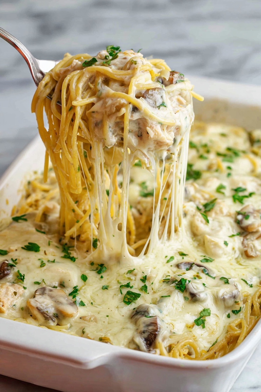 A white baking dish filled with creamy baked spaghetti is shown, featuring one thick layer of pasta mixed with mushrooms and shredded chicken, all covered with a smooth, melted white cheese sauce. The top layer is sprinkled with chopped fresh green herbs. A silver serving spoon lifts a portion of the spaghetti noodles, showing the soft texture and strands of melted cheese stretching from the dish. The background has a white marbled texture. Photo taken with an iphone --ar 2:3 --v 7 - Creamy Chicken Tetrazzini Bake, Chicken Tetrazzini casserole, cheesy chicken pasta bake, easy chicken pasta recipe, comforting chicken bake