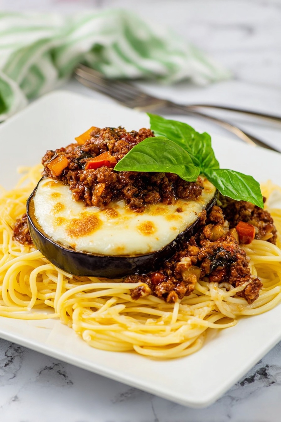 The dish shows a pile of yellow spaghetti noodles spread in a loose mound on a white square plate with rounded edges. On top of the noodles, there are slices of cooked eggplant with a glossy purple skin and soft interior, covered by a layer of melted, slightly browned white cheese. Between the eggplant layers, there are pieces of browned ground meat mixed with small bits of red tomatoes and mushrooms, adding texture and color. The top is garnished with fresh green basil leaves, adding a bright, leafy contrast. The plate sits on a white marbled surface with an orange and white striped cloth and a fork and knife placed behind it near the upper left edge. Photo taken with an iphone --ar 2:3 --v 7 - Eggplant Parmesan Spaghetti with Meat Sauce, Eggplant Parmesan pasta, Italian eggplant spaghetti, hearty eggplant pasta recipe, meat sauce spaghetti