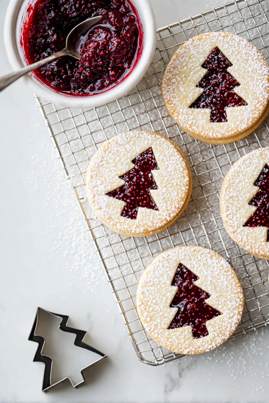 The image shows a cooling rack on a white marbled surface with four round layered cookies arranged on it and nearby. Each cookie has two layers: a light beige cookie base on the bottom, a layer of deep red raspberry jam in the middle, and a top cookie layer with a Christmas tree shape cut out, revealing the jam below. The top layer is dusted with white powdered sugar, creating a delicate snowy look. To the left of the rack is a small white bowl filled with thick, dark red raspberry jam with visible seeds, and a silver spoon inside. Near the bottom left corner, there is a small metal cookie cutter in the shape of a Christmas tree. photo taken with an iphone --ar 2:3 --v 7 - Raspberry Linzer Cookies, butter biscuit cookies with raspberry jam, fruit-filled sandwich cookies, homemade Linzer cookies, easy raspberry cookie recipe