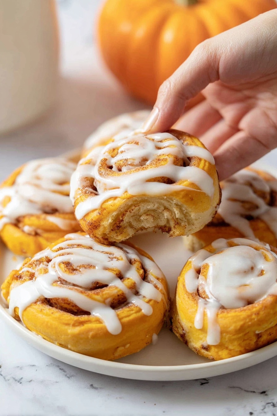 A white plate filled with six bright orange spiral rolls, each topped with a thick drizzle of white icing. The rolls have multiple visible layers with a soft, doughy texture and a cinnamon-spice swirl inside that adds a speckled light brown pattern. A woman's hand is gently lifting one roll from the plate, showing more of its smooth icing on the top center. The background is a white marbled texture with a small orange pumpkin blurred in the back. photo taken with an iphone --ar 2:3 --v 7 - Pumpkin Cinnamon Rolls with Cream Cheese Glaze, pumpkin cinnamon rolls, fall cinnamon roll recipes, easy pumpkin pastry, cozy fall baking ideas