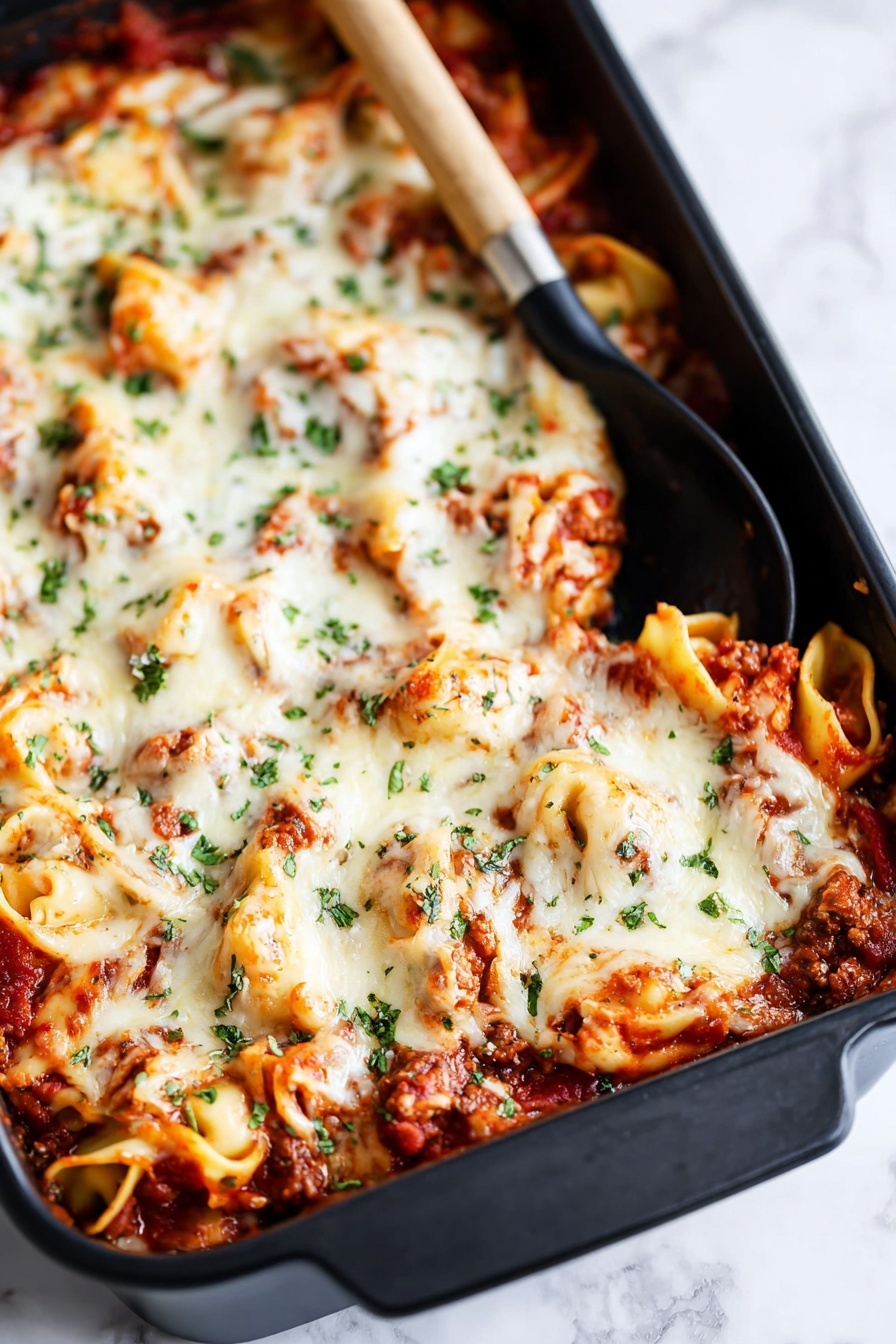 The image shows a large black baking dish filled with a layered pasta bake. The bottom layer has visible tomato sauce with small chunks of meat, rich red in color. On top of this is a thick layer of melted white cheese, which looks creamy and slightly browned in some spots. Scattered green herbs, probably parsley or basil, are sprinkled over the cheese, adding color contrast. There are curled pasta pieces, possibly tortellini, peeking through the cheese layer, coated in sauce and cheese. A black spoon with a wooden handle rests inside the dish near the top corner. The dish is placed on a white marbled surface. Photo taken with an iphone --ar 2:3 --v 7 - Baked Tortellini Casserole with Cheese, cheesy tortellini bake, easy tortellini casserole, baked pasta recipes, comfort food dinner