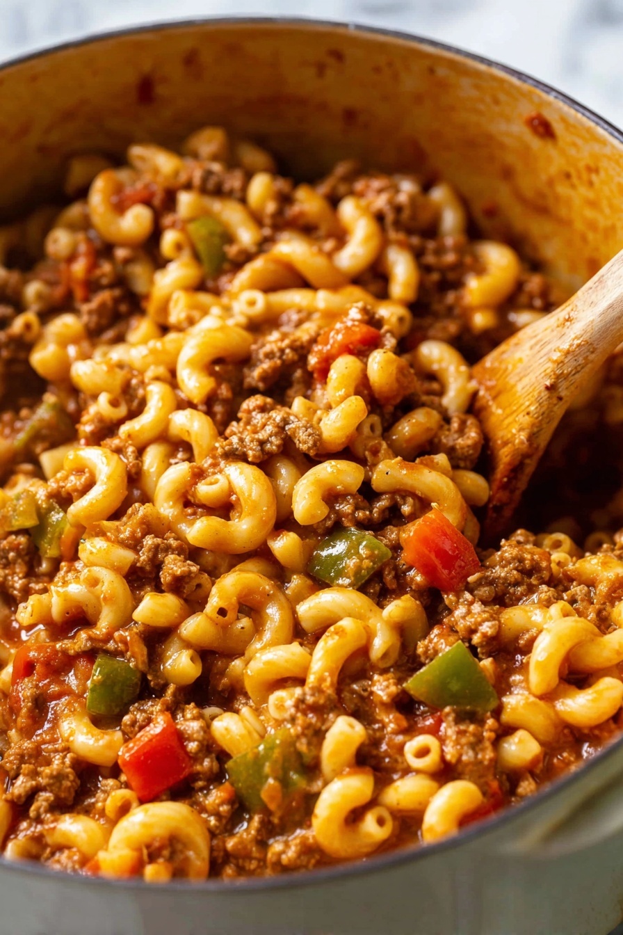 The image shows a close-up of a pot filled with elbow macaroni pasta mixed with ground meat, diced tomatoes, and chopped green bell peppers. The pasta is soft and coated with a rich reddish-brown sauce. The ground meat is crumbled small and evenly spread throughout the dish. Bright red tomato pieces and small chunks of green bell peppers add pops of color. A wooden spoon is stirring the mixture on the right side. The pot has a soft brown inside texture, and the background is a white marbled surface. photo taken with an iphone --ar 2:3 --v 7 - American Chop Suey, easy American Chop Suey recipe, comfort food recipes, quick weeknight dinners, hearty pasta dishes