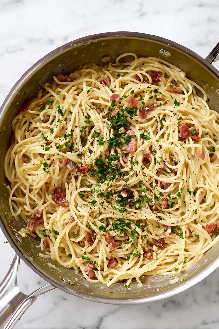 A silver metal pan filled with spaghetti noodles mixed with small pieces of reddish-brown bacon and finely chopped green parsley sprinkled on top. The pasta has a light cream sauce coating, and tiny black pepper bits are scattered throughout. The pan is placed on a white marbled surface. Photo taken with an iphone --ar 2:3 --v 7 - Easy Spaghetti Carbonara, quick Italian pasta, creamy carbonara without cream, simple pasta recipes, authentic spaghetti carbonara