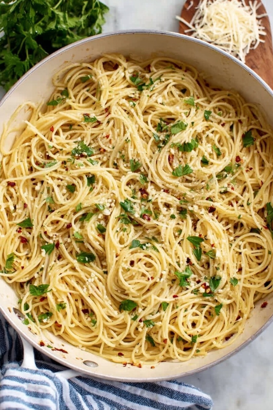 A white pan filled with a single layer of thin spaghetti pasta cooked and mixed with small bits of white garlic and red chili flakes spread throughout. Fresh green parsley leaves are scattered on top, adding a touch of color and freshness. The pan rests on a white marbled surface next to a blue and white striped cloth, with fresh parsley and some shredded cheese partially visible in the background. Photo taken with an iphone --ar 2:3 --v 7 - Garlic Olive Oil Spaghetti, easy garlic pasta, simple Italian pasta, quick spaghetti dinner, flavorful garlic olive oil pasta