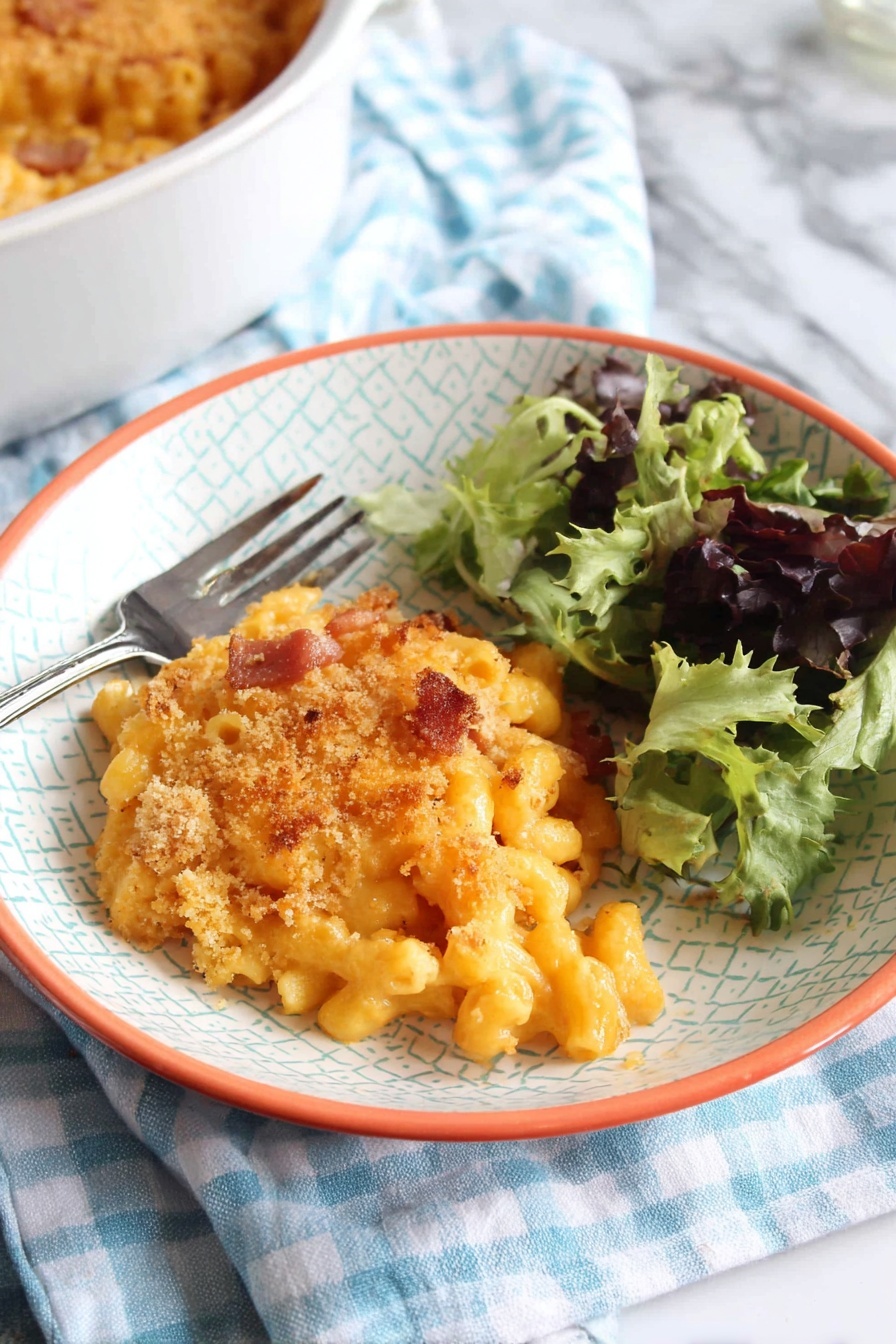 A white bowl with a light geometric pattern and orange rim holds a serving of baked macaroni and cheese topped with a golden breadcrumb crust with some browned spots. The macaroni pasta under the crust is creamy and orange, with small pieces of browned bacon or ham mixed inside. To the right side of the bowl is a small fresh salad of mixed green leaves, some dark purple and others bright green with curly texture. A silver fork rests on the left edge of the bowl. The bowl sits on a blue and white checkered cloth over a white marbled surface. In the bottom left corner, part of a white round baking dish filled with more macaroni and cheese is visible. photo taken with an iphone --ar 2:3 --v 7 - Chorizo Mac and Cheese Bake, spicy mac and cheese, cheesy chorizo pasta bake, comforting baked pasta, easy chorizo pasta recipes