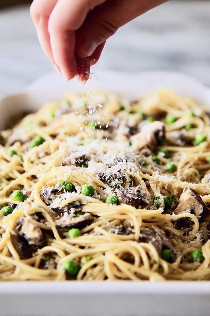 A round serving of baked pasta with visible noodles, small green peas, and bits of light beige chicken arranged in the center of a shiny white plate with a blue rim. The top layer is sprinkled with golden toasted breadcrumbs, adding a rough texture. A silver fork is placed on the right side of the plate, its tines partly under the pasta. The plate rests on a white marbled surface, and in the blurry background, there is a white baking dish filled with more of the same pasta bake. The light is soft and natural, showing the creamy and slightly browned surface of the pasta. photo taken with an iphone --ar 2:3 --v 7 - Turkey Tetrazzini Casserole, Turkey casserole recipe, cheesy turkey pasta bake, creamy turkey casserole, comfort food with turkey