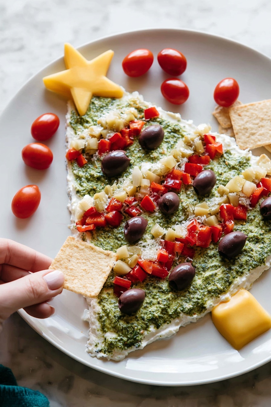 The image shows a white plate with a Christmas tree-shaped layered dip. The first layer is a smooth, white creamy base covering the entire tree shape. The second layer is a rough, green spread resembling pesto, filling most of the tree shape except the edges. On top, there are several red diced pepper pieces forming three diagonal lines across the tree. Small dark purple olive slices are scattered evenly over the green layer. There are small chunks of pale yellow artichoke hearts mixed in with the red peppers. Bright red cherry tomatoes decorate the edges, with a large yellow star-shaped piece placed at the top of the tree. A woman's hand is holding a square chip near the plate on a white marbled surface photo taken with an iphone --ar 2:3 --v 7 - Christmas Tree Bean Dip with Pesto and Veggies, festive holiday appetizer, healthy Christmas vegetable dip, easy holiday party dip, colorful veggie dip