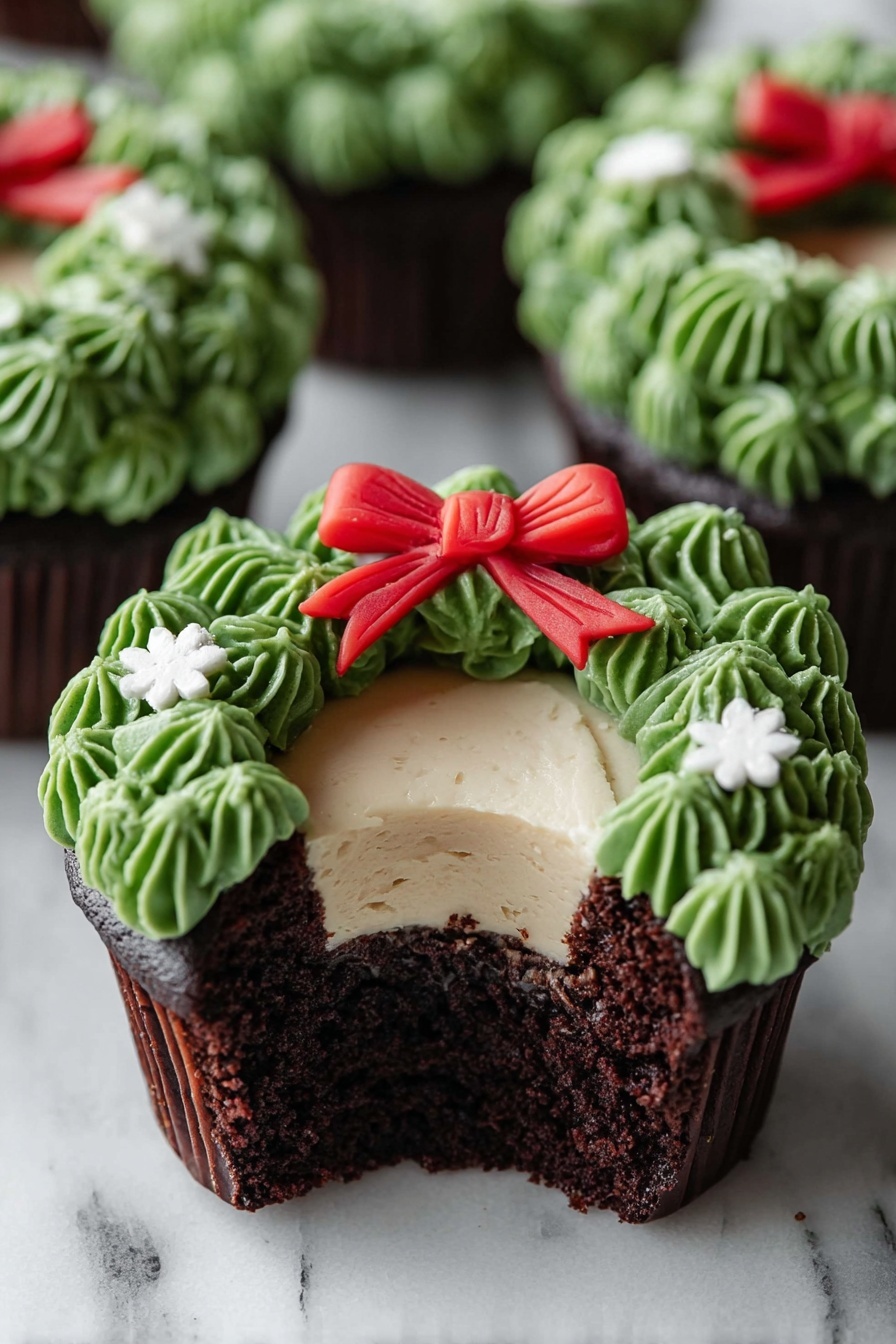A chocolate cupcake with three visible layers is shown on a white marbled surface. The bottom layer is dark, moist chocolate cake, the middle layer is a smooth light cream filling, and the top layer is decorated with green frosting piped to look like leaves forming a wreath around the cream. A small red bow made of fondant sits at the top center of the green wreath, and tiny white flower-shaped decorations are placed on the green frosting. The cupcake is partially eaten, showing the inside layers clearly. Other similar cupcakes are blurred in the background. Photo taken with an iphone --ar 2:3 --v 7 - Chocolate Wreath Cupcakes, festive holiday cupcakes, chocolate cupcake recipe, wreath design cupcakes, easy holiday dessert