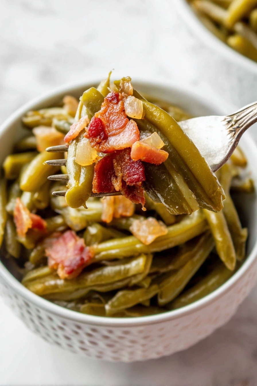 A white bowl with a pattern holds cooked green beans layered at the bottom, soft and shiny with a slightly wrinkled texture. On top, small chunky pieces of browned bacon with a reddish-brown tone and a bit of translucent cooked onion are mixed in. A fork lifts some green beans and bacon from the bowl, showing the layers clearly, with the vegetables still moist and the bacon crispy in places. The background is a white marbled surface. photo taken with an iphone --ar 2:3 --v 7 - Slow Cooker Bacon Green Beans, green beans with bacon, easy green bean side dish, smoky green beans recipe, crock pot green beans
