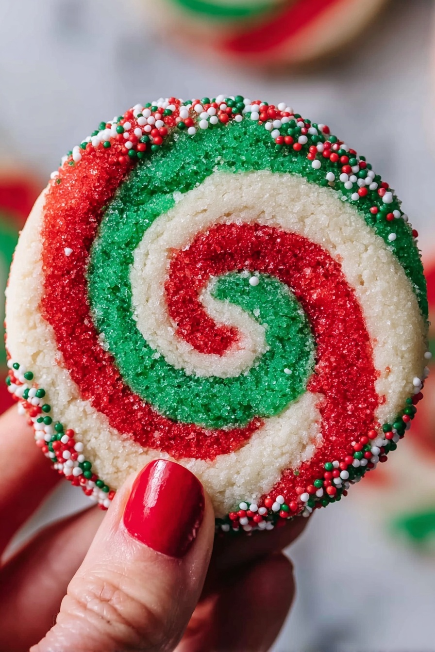 A round cookie with a red, white, and green swirl pattern that forms a spiral from the center to the edges. The outer edge of the cookie is coated with small red, white, and green round sprinkles. A woman's hand with red nail polish holds the cookie against a blurred background, and the surface under the cookie is white marbled texture. photo taken with an iphone --ar 2:3 --v 7 - Colorful Swirled Christmas Cookies, festive holiday cookies, easy Christmas cookie recipes, colorful holiday cookies, swirl cookie ideas