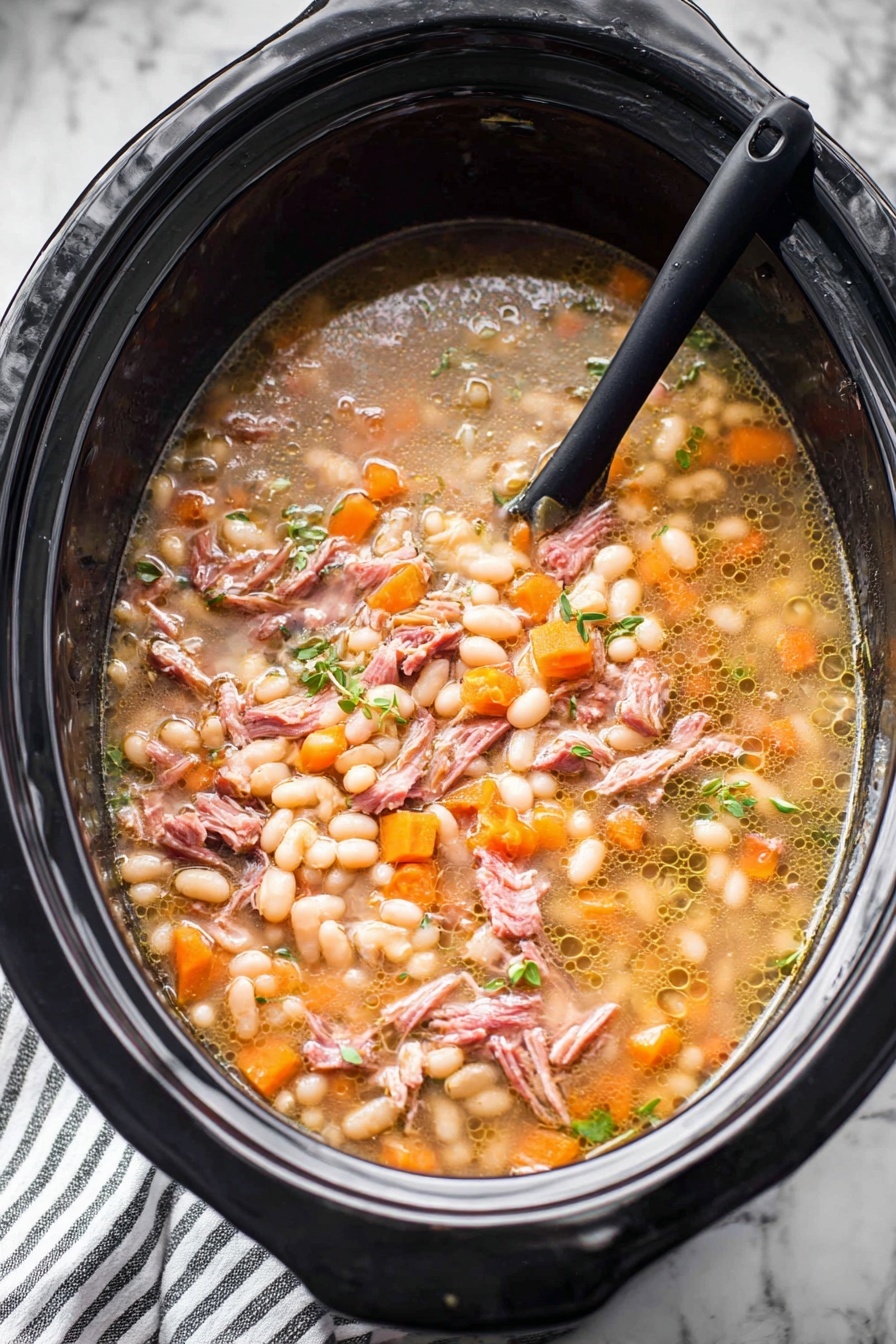 A large black slow cooker filled with a stew that has several layers and textures. The base layer shows a light brown broth with small bubbles of oil floating on top. Floating in the broth are many small, soft white beans, many small orange carrot cubes, and small bits of translucent onions. There are also shredded pieces of pinkish-brown cooked meat spread evenly throughout. Small green herbs are scattered on top, adding a fresh touch. A black spoon is partially submerged on the left side, resting inside the slow cooker. The slow cooker sits on a white marbled surface with a striped cloth partially visible below. Photo taken with an iphone --ar 2:3 --v 7 - Hearty Ham and Bean Soup, hearty ham and bean soup, easy ham and bean soup, comforting bean soup recipe, smoky ham bean stew